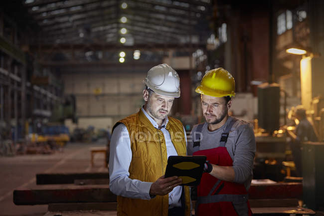 Capataz masculino e engenheiro usando tablet digital na fábrica escura — Fotografia de Stock