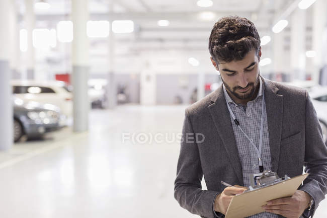 Car salesman writing on clipboard in car dealership auto repair shop — Stock Photo