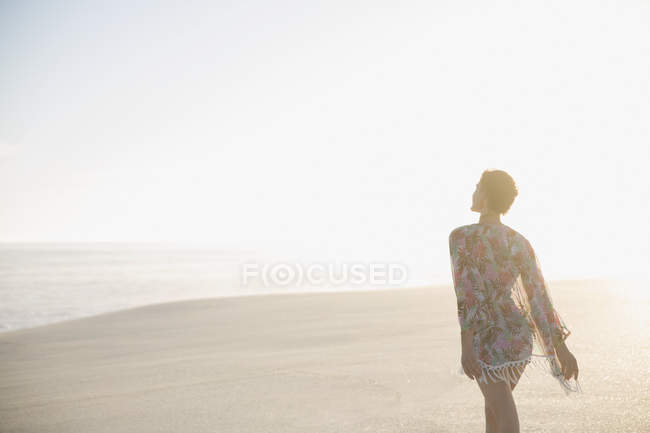 Serene woman in swimsuit coverup walking on sunny summer beach — Stock Photo