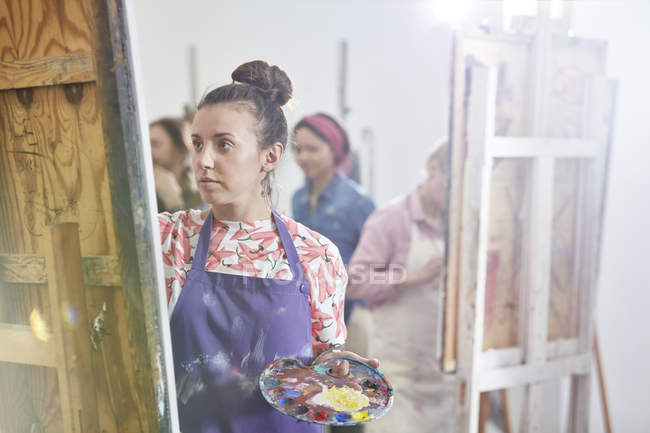 Focused female artist with palette painting at easel in art class studio — Stock Photo