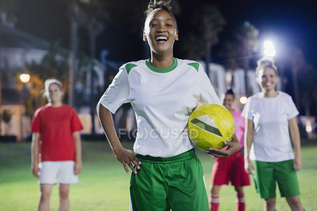 Portrait confident, laughing young female soccer player practicing on field at night — Stock Photo