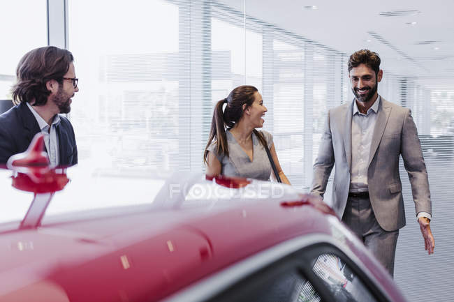 Продавець автомобілів і посміхаючись пара клієнтів, які шукають на новий автомобіль в дилерському автосалон — стокове фото
