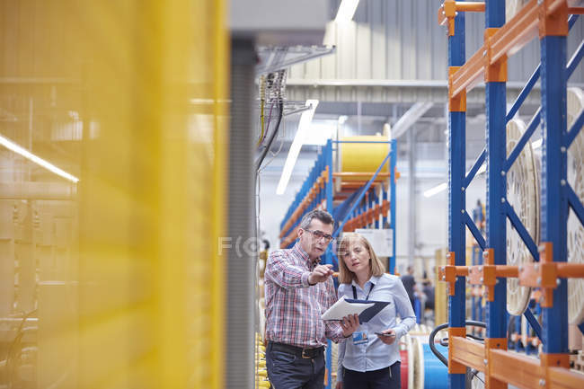 Male and female managers with clipboard talking in fiber optics factory — Stock Photo
