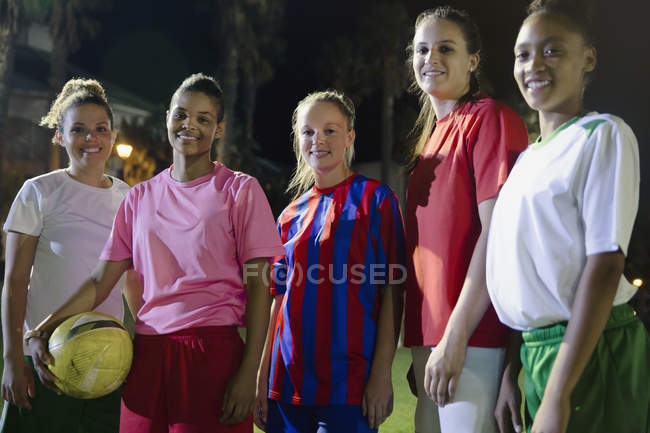 Portrait smiling, confident young female soccer teammates with ball on field at night — Stock Photo