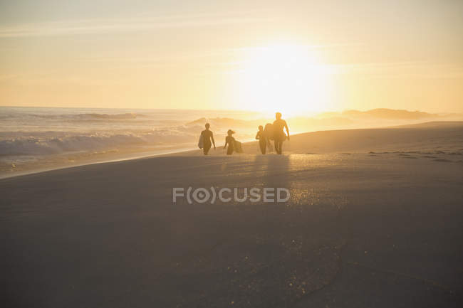 Silueta familia caminando en la soleada playa del atardecer de verano - foto de stock