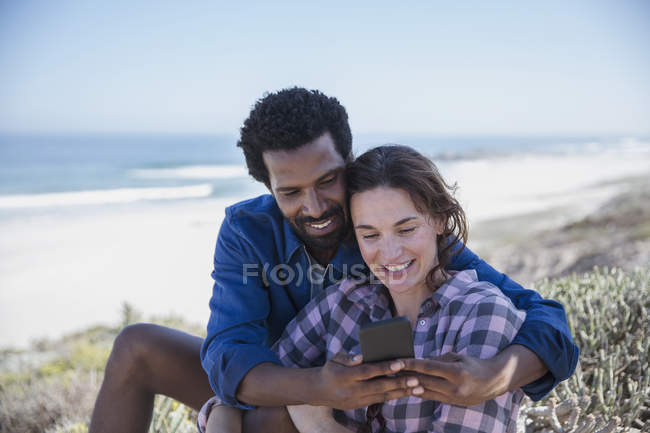 Улыбающаяся многонациональная пара делает селфи с мобильником на летнем пляже — стоковое фото
