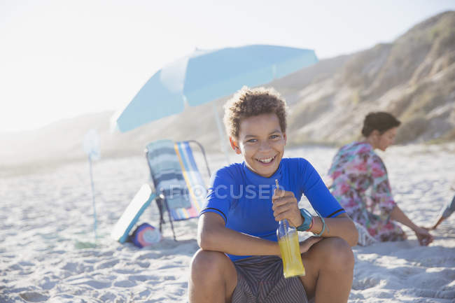 Retrato sorrindo, menino confiante beber suco na praia ensolarada verão — Fotografia de Stock