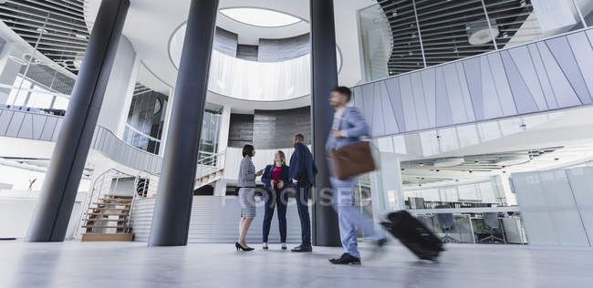 Empresários falando e puxando mala no lobby de escritório arquitetônico e moderno — Fotografia de Stock