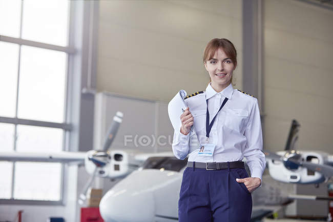 Portrait confident pilot with paperwork in airplane hangar — Stock Photo