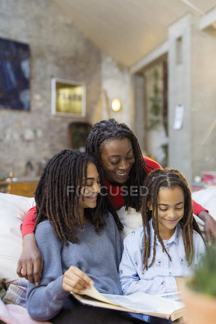Mãe e filhas sorridentes olhando para o álbum de fotos no sofá — Fotografia de Stock