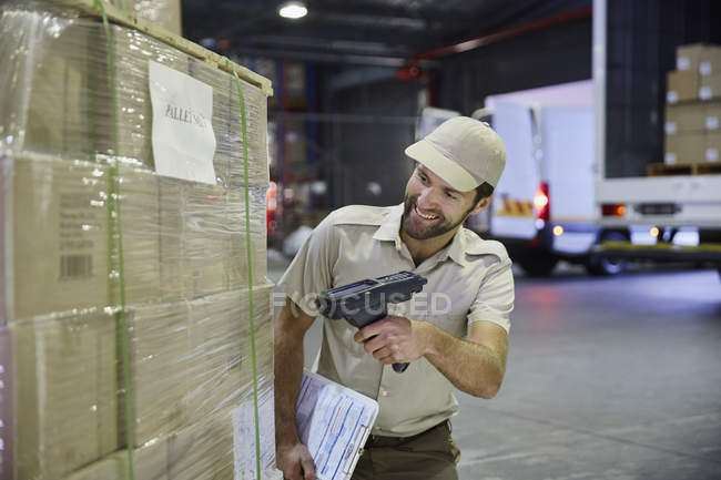Camionero trabajador escaneando paleta de cajas de cartón en el muelle de carga de almacén de distribución - foto de stock