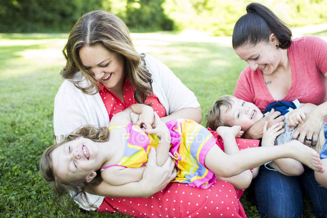 Playful lesbian mothers playing, tickling children in grass — Stock Photo