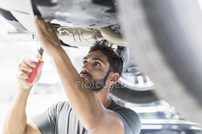 Mécanicien masculin concentré travaillant sous voiture dans un atelier de réparation automobile — Photo de stock