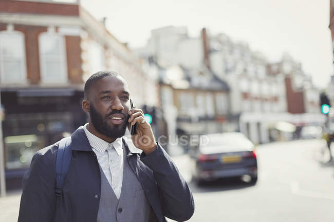 Homme d'affaires parlant sur un téléphone portable dans une rue urbaine ensoleillée — Photo de stock