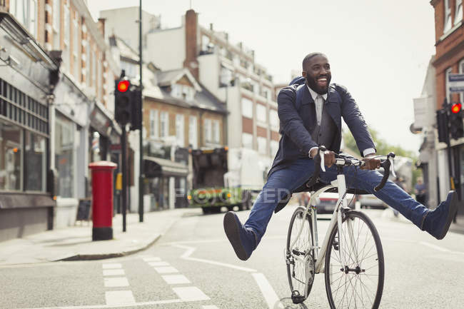 Caucho Disminución compensar Juguetón joven hombre de negocios conmutando, montar en bicicleta en la  calle urbana — Adultos jóvenes, etnia africana - Stock Photo | #202760118
