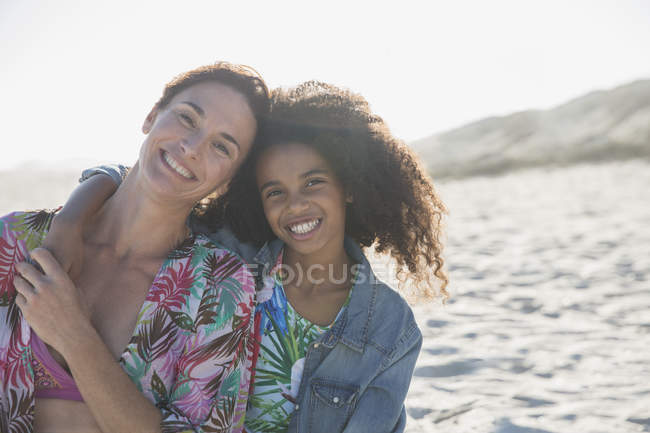 Портрет улыбается, уверенная мать и дочь обнимаются на солнечном летнем пляже — стоковое фото