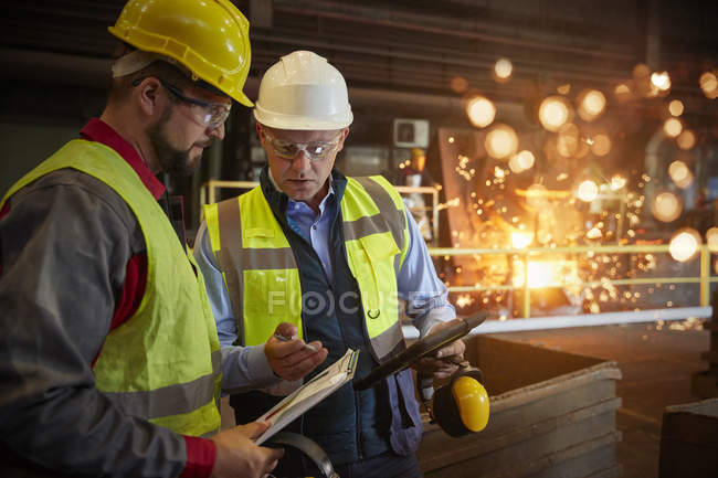Superviseur et métallurgiste avec presse-papiers parlant dans une aciérie — Photo de stock