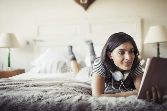 Frau mit Kopfhörer entspannt sich im Bett mit digitalem Tablet — Stockfoto