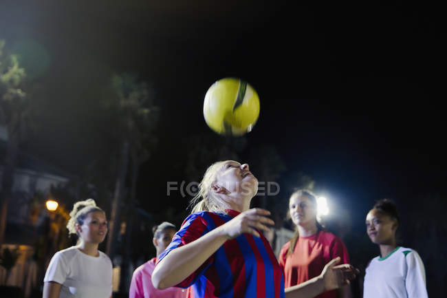 Young female soccer players practicing at night, heading the ball — Stock Photo