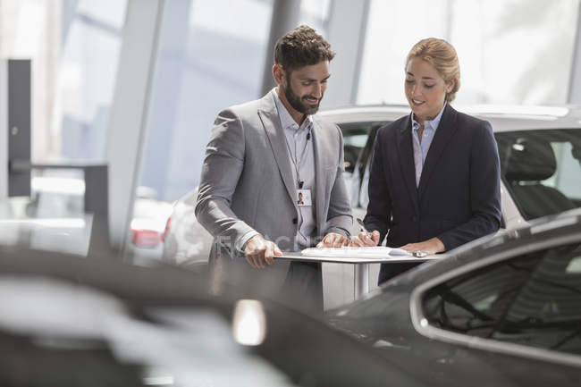 Vendedor de automóviles y cliente femenino revisando el papeleo del contrato financiero en la sala de exposición de concesionarios de automóviles - foto de stock