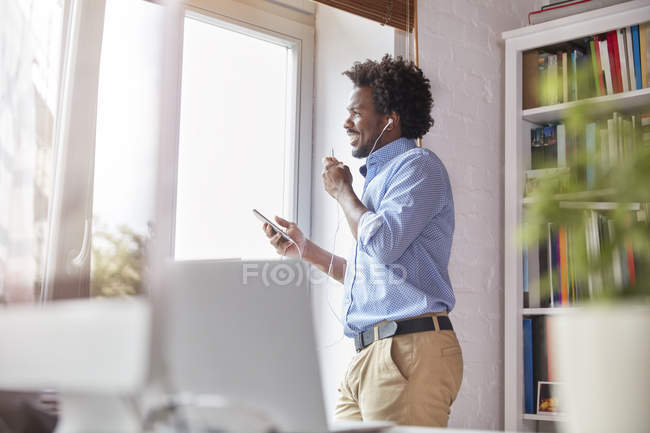 Empresário sorridente falando no celular com fones de ouvido no escritório — Fotografia de Stock