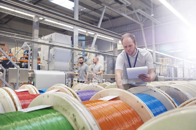Мужчина с планшетом, проверяющий многоцветные катушки на волоконно-оптическом заводе — стоковое фото