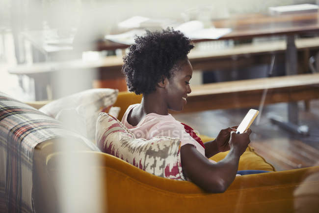 Femme souriante textos avec téléphone intelligent sur le canapé du salon — Photo de stock