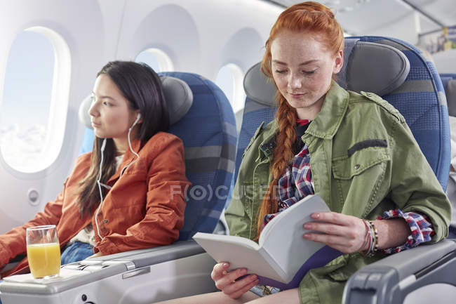 Young woman reading book on airplane — Stock Photo