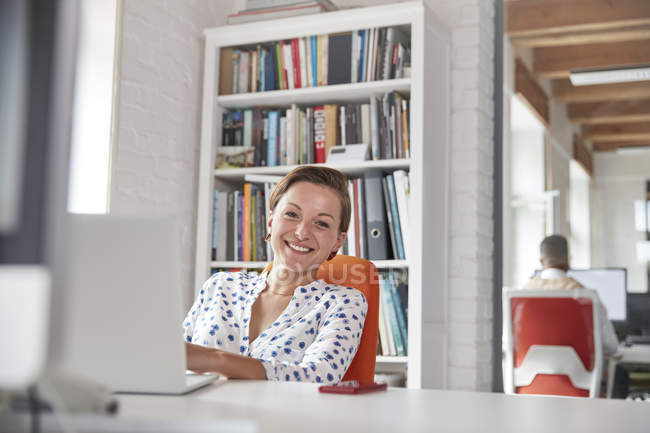 Портрет улыбается, уверенная деловая женщина, работающая за ноутбуком в офисе — стоковое фото
