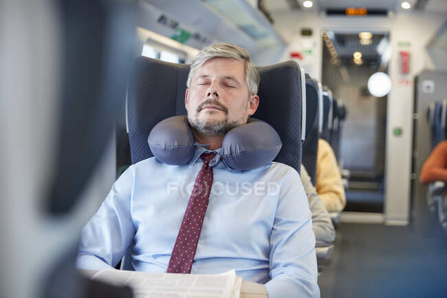 Уставший бизнесмен с подушкой на шее спит в пассажирском поезде — стоковое фото