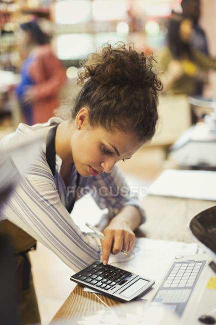 Female cashier using calculator in shop — Stock Photo