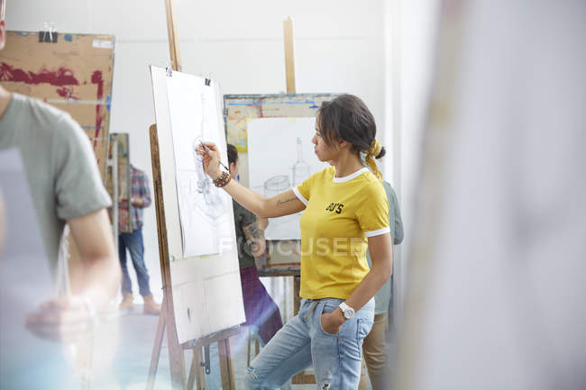 Female artist sketching at easel in art class studio — Stock Photo