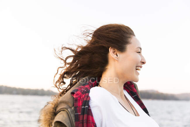 Lächelnde, unbeschwerte Frau am windigen Seeufer — Stockfoto