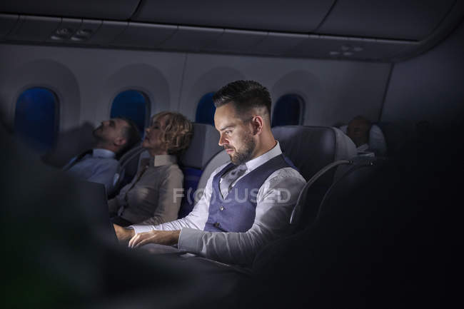 Бізнесмен, що працює на ноутбуці на нічному літаку — стокове фото