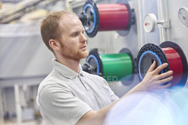 Travailleur masculin changeant de bobine dans une usine de fibre optique — Photo de stock