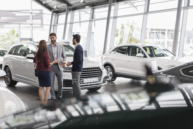 Car salesman talking to couple customers in car dealership showroom — Stock Photo