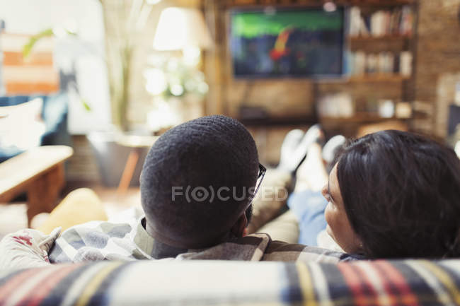 Молодая пара отдыхает, смотрит телевизор на диване в гостиной — стоковое фото