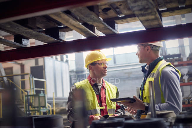 Trabajadores siderúrgicos con tableta digital hablando en acerías - foto de stock