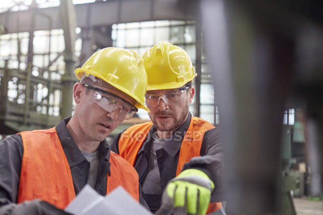 Male workers discussing paperwork in factory — Stock Photo