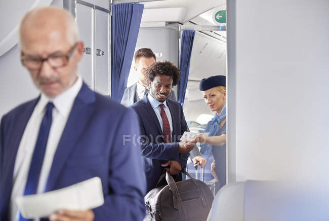 Asistente de vuelo ayudando a hombre de negocios con tarjeta de embarque en el avión - foto de stock