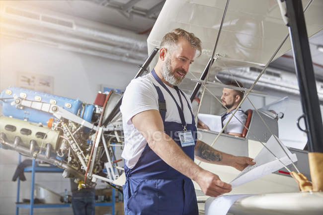 Чоловічий інженер-механік розглядає плани на літаку в ангарі — стокове фото
