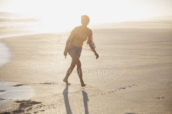 Улыбающаяся женщина идет по солнечному песчаному летнему пляжу — стоковое фото