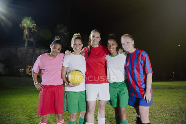 Portrait souriant, confiant jeunes coéquipières de soccer avec ballon sur le terrain la nuit — Photo de stock
