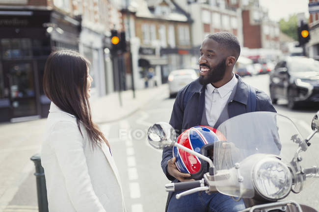 Smiling young businessman on motor scooter talking to friend on urban street — Stock Photo