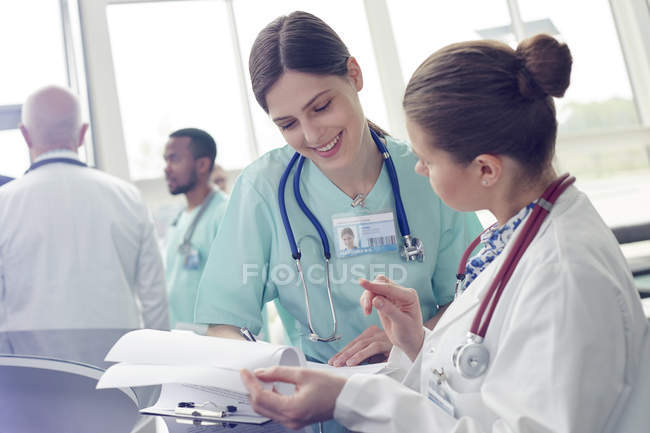 Médica e enfermeira sorridente com prancheta conversando no hospital — Fotografia de Stock
