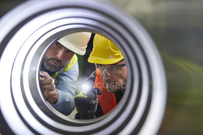 Serious male engineers with flashlights examining steel pipe — Stock Photo