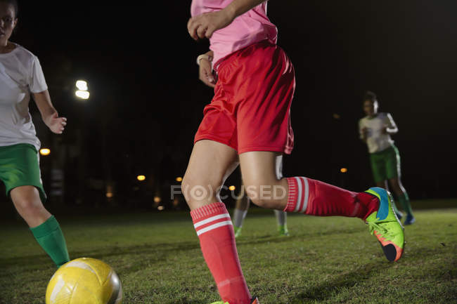 Jóvenes jugadoras de fútbol jugando en el campo por la noche, corriendo por la pelota - foto de stock