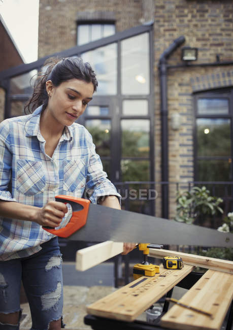 Young woman with saw cutting wood on patio — Stock Photo