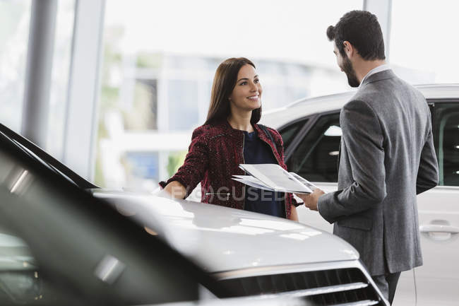 Vendedora de carros mostrando brochura para o cliente masculino no showroom concessionária de automóveis — Fotografia de Stock