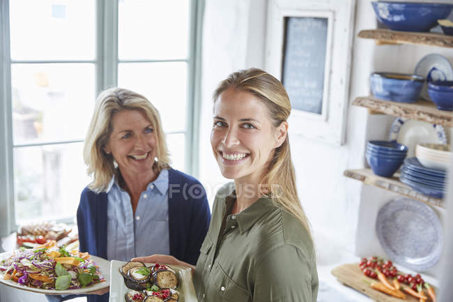 Портрет улыбающейся матери и дочери, подающих еду — стоковое фото